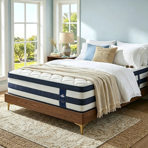 A resspry mattress on a wooden bed frame styled in a bright bedroom with white bedding, a beige throw blanket, blue pillows, and large windows with outdoor views.